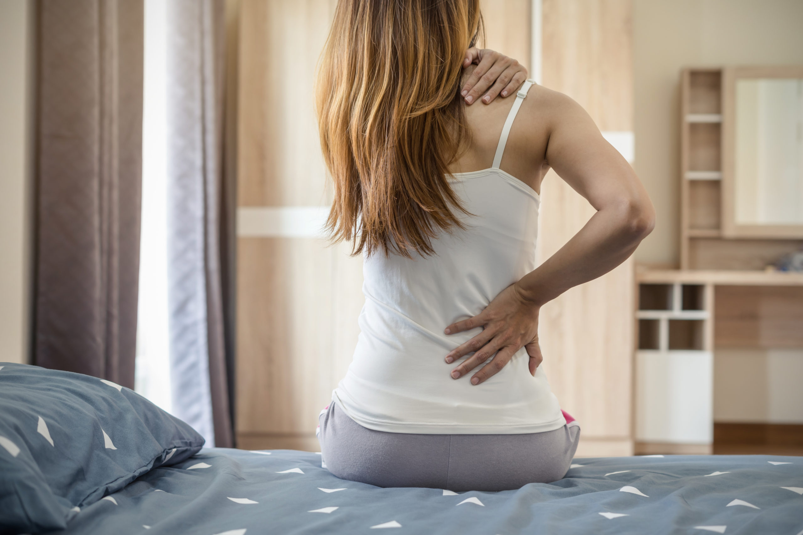 Woman suffering from back ache on the bed, healthcare and problem concept