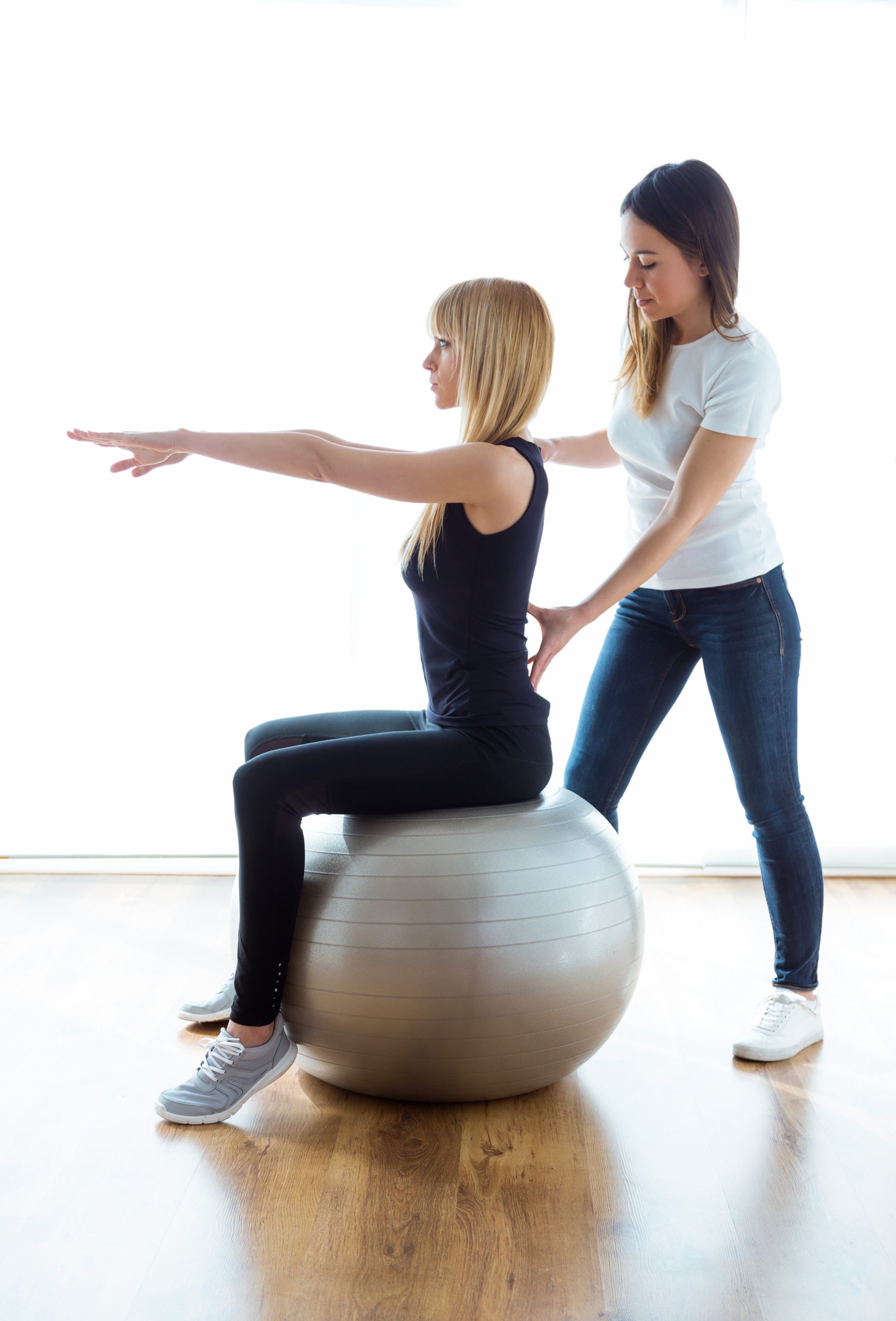 Shot of physiotherapist helping patient to do exercise on fitness ball in physio room.