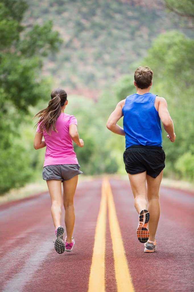 Running training runners jogging on road outside in rear view running away from camera in nature landscape. Sport fitness and healthy lifestyle concept with two people, man and woman.