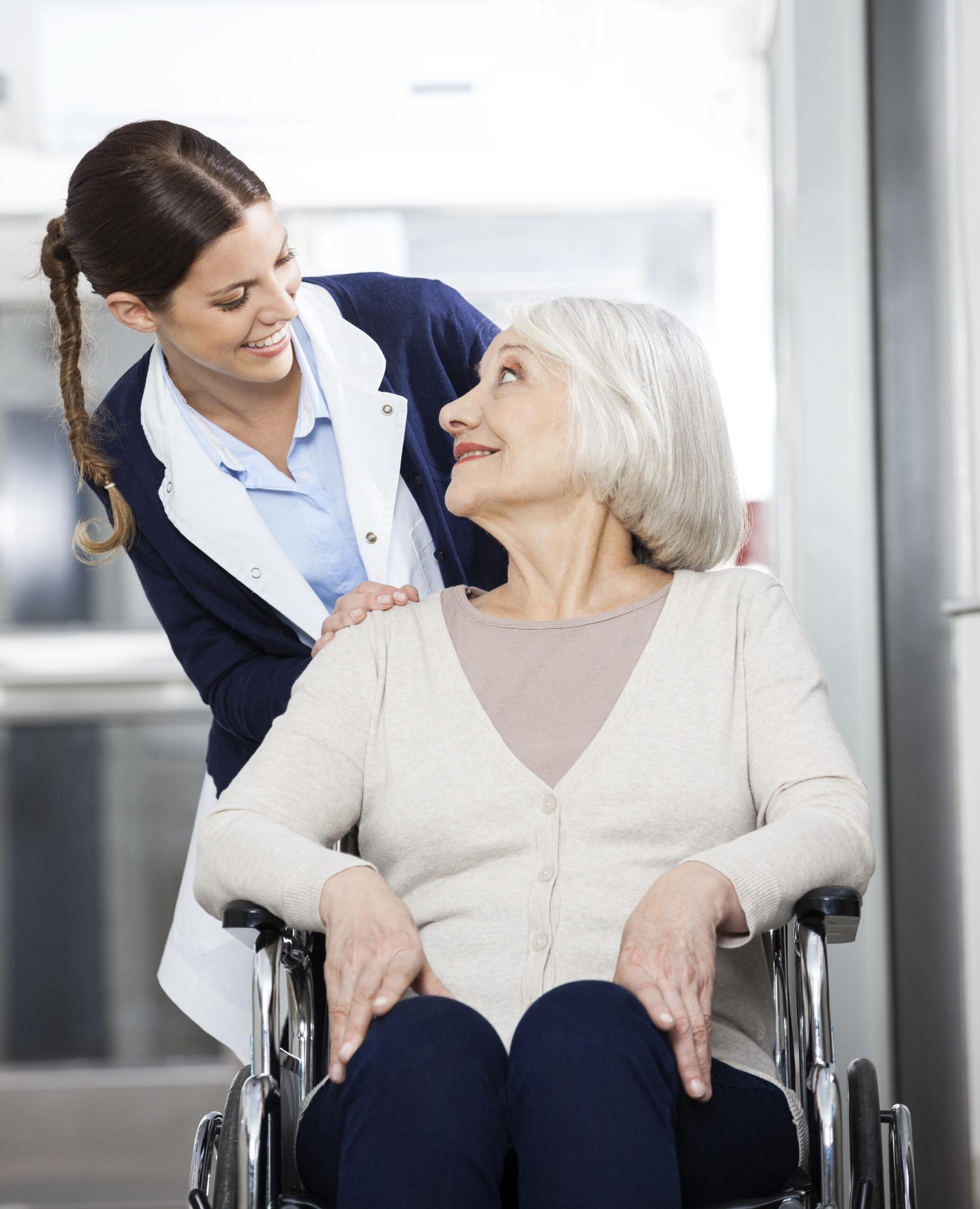 Happy female physiotherapist looking at senior patient sitting in wheelchair in rehab center