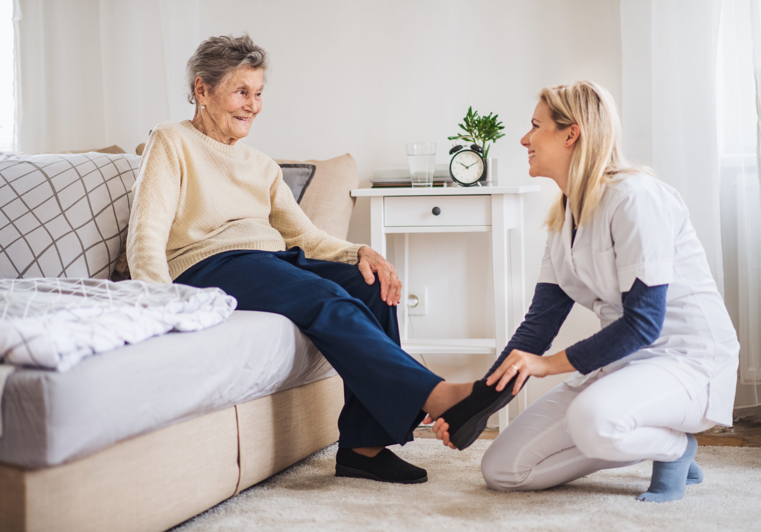 A young health visitor putting on slippers on a senior woman at home at Christmas time.